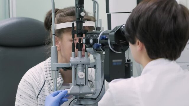 Woman doctor is viewing through ophthalmoscope in eyes of patient in ophthalmologic clinic. Professional inspection of vision