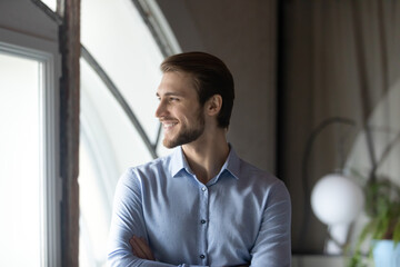 Successful smiling young man corporate employee boss team leader satisfied with professional achievements career growth standing close to window looking forward creating business vision strategy plan © fizkes