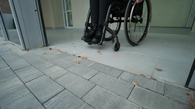 Disabled woman in wheelchair at home comes out to modern office building