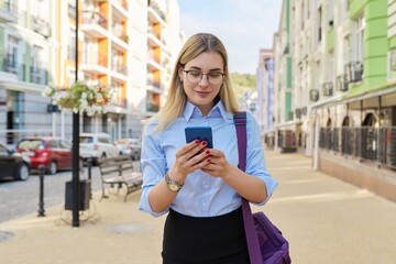 Fototapeta premium Business woman in glasses in blue shirt with laptop bag using smartphone