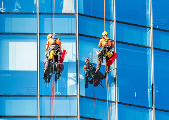 Washers wash the windows of modern skyscraper. Window cleaner working on a glass facade of modern...