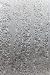 Natural drops of water flow down the glass, high humidity in the room, condensation on the glass window. Neutral colors. Vertical photo orientation