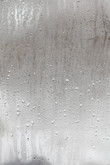 Natural drops of water flow down the glass, high humidity in the room, condensation on the glass window. Neutral colors. Vertical photo orientation - obrazy, fototapety, plakaty