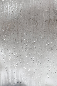 Natural drops of water flow down the glass, high humidity in the room, condensation on the glass window. Neutral colors. Vertical photo orientation