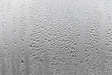 Close up water drop on grey background, misted glass with droplets of water draining down. Dripping Condensation