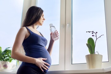 Young beautiful pregnant woman drinking water from bottle