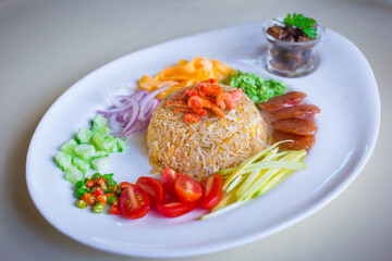 Shrimp paste fried rice is served with sweet pork, sliced fried egg, fried dry shrimp and Thai sausage, chopped red onion, chili and raw mango as topping. It is a Thai cuisine, Thai food.