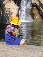 Women wear traditional Thai costumes and yellow hats. Sitting by the waterfall