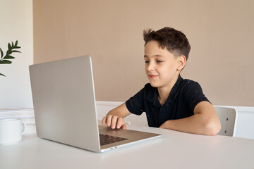Schoolboy boy sitting at a desk with a laptop, writes school lessons during homework. High quality photo