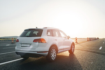 White crossover car on empty asphalt road at sunrise