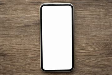 Smartphone with blank mock up screen is on top of wood table. Top view, flat lay.