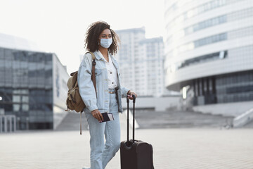 Young woman tourist holding passport and ticket, girl wearing protective face mask in a city,...