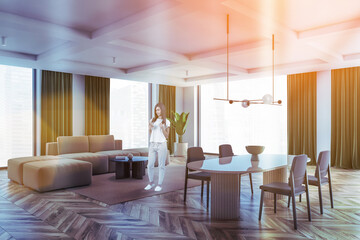 Living room with brown and grey furniture and windows, woman with phone