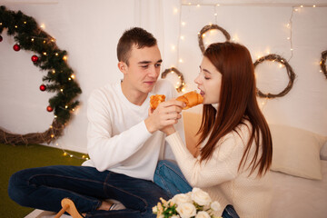 A young happy couple in love eats in a photo studio. The guy and the girl are funny feeding each other. Posing for models in a studio for Christmas Family dinner for New Year's Eve, Breakfast in bed