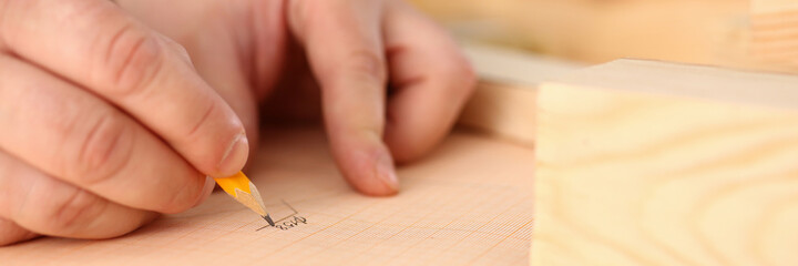 Professional woodworker using pencil while drawing scheme on piece of wood