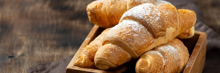 Croissants. Croissants and cappuccino in a wooden box on a brown background. French breakfast. Banner	