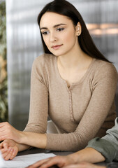 Friendly young businessman and programmer in a green shirt is working on computer, while sitting together at the desk with a female colleague in a modern office. Focus on woman. Concept of successful