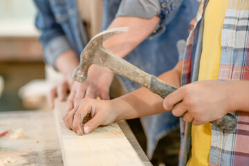 Close up father teaches son to hammer nails in the workshop
