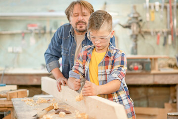 Carpenter teaches young boy to plan wood in a carpentry workshop