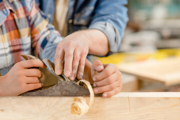 Close up father teaches son to plan a wooden block. Empty space for text