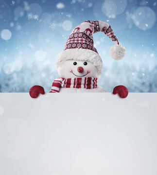 Happy snowman in the winter scenery behind the blank advertising banner with copy space