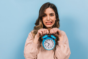 Funny young lady posing with big clock. Studio shot of winsome caucasian girl standing on blue...