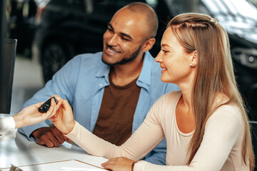 Salesperson giving key to buyer in a car salon