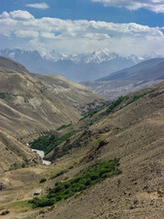 Fototapeta premium Pamir river gorge in the high-altitude desert between Afghanistan and Tajikistan in the Wakhan Corridor with Hindu Kush snow-capped mountain range in the background, Gorno-Badakshan