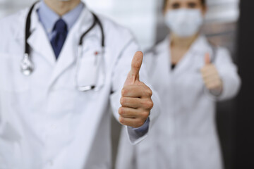 Unknown man-doctor and woman standing straight as a team and showing Ok sign with thumbs up in modern clinic. Medicine concept during Coronavirus pandemic. Covid 2019