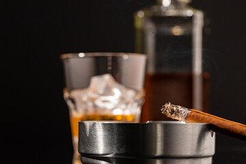 Glass of whisky and lighted cigar on black background