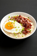 Homemade Cheesy Bacon Savory Oatmeal Bowl on a black background, side view. Close-up.