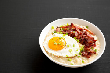 Homemade Cheesy Bacon Savory Oatmeal Bowl on a black background, side view. Copy space.