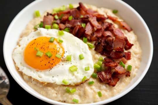 Homemade Cheesy Bacon Savory Oatmeal Bowl On A Black Background, Side View. Close-up.