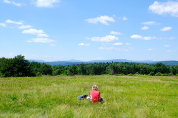 Lonely woman is sitting on meadow in mountains and planning trip. Viewpoint on Wysokie (High) in Low Beskid Mountains, around Krempna, Poland