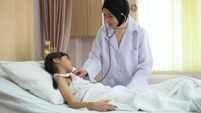 Arab doctor woman examining  girl patient body by stethoscope on bed in hospital