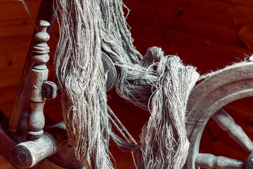 Spun linen flax yarns on an ancient wooden spinning wheel made of an oak in a room with wooden...