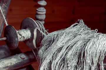 Spun linen flax yarns on an ancient wooden spinning wheel made of an oak in a room with wooden...