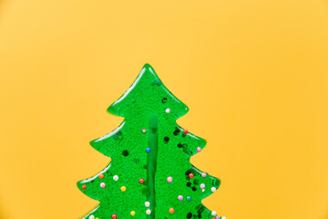 Lollipop in the shape of a Christmas tree close-up on a yellow background.