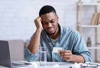 African Man Suffering From Headache Reading Pills Instruction At Workplace