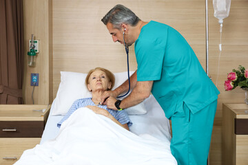 Doctor or assistance staff talking with an elder patient woman while using stethoscope and sleep on bed in the hospital