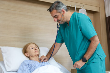 Obraz premium Doctor or assistance staff talking with an elder patient woman while using stethoscope and sleep on bed in the hospital