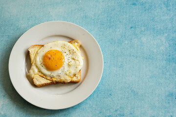 toast with fried eggs on white plate, against blue background