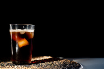 iced coffee with milk and ice cubes in a glass against black background. Space for text