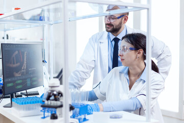 Naklejka premium Two scientists are working together in laboratory using computer at workplace. Team of researchers doing pharmacology engineering in sterile lab for healthcare industry.