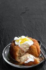 Rum baba decorated with whipped cream on black stone background