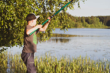 A teenage European boy fishing with a fishing rod in the summer. Fishing on the river in Russia.