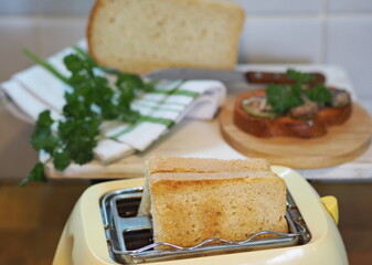 Two pieces of toast in a toaster in the kitchen against the background of a cutting board, bread and kitchen napkin and a sandwich on toast. Healthy fancy breakfast food.