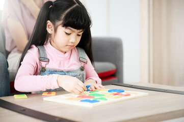 Asian daughter with parent playing toy puzzle on table at home. Kid girl is smiling and enjoy activity leisure