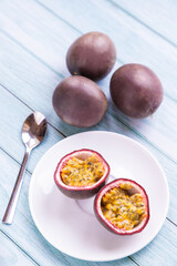 passion fruit in a plate on a blue wooden table, one is cut and ready-to-eat with a spoon - 396087894