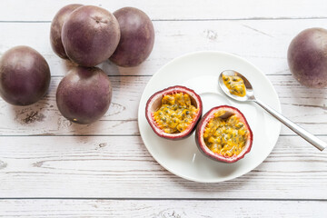 ripe passion fruit in a plate on a white wooden table, one is cut and ready-to-eat with a spoon - 396088021